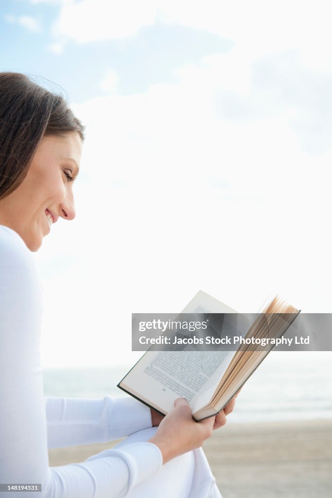 Hispanic woman reading book on beach