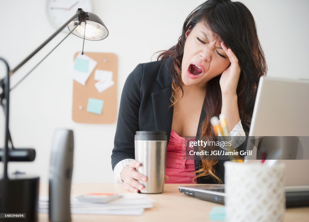 Pacific Islander businesswoman yawning at desk