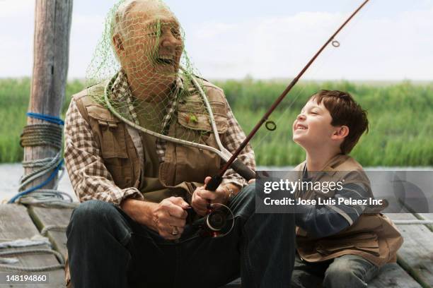 caucasian boy putting fishing net over grandfather's head - seniors having fun with grandson stockfoto's en -beelden