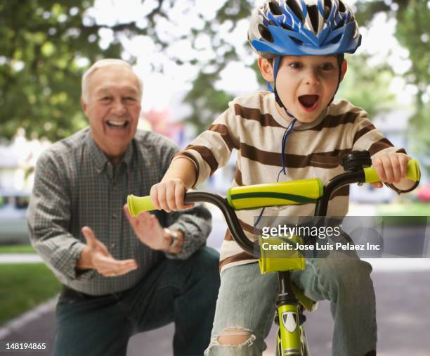 caucasian man teaching grandson to ride a bicycle - family riding bikes with helmets stock pictures, royalty-free photos & images