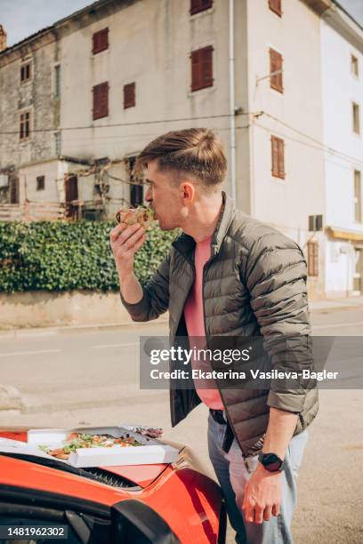 man eating pizza on the hood of a red car in a parking lot male hands - zagreb food stock pictures, royalty-free photos & images