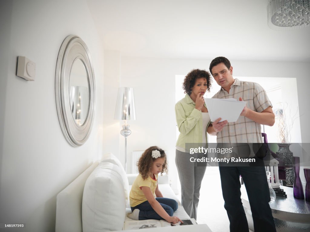 Couple discussing energy bills while daughter plays on sofa in living room