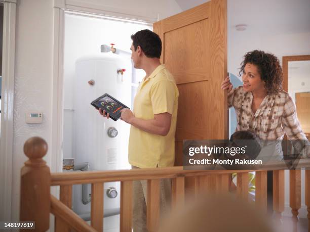 mother and son watching father check hot water tank with energy application on digital tablet - boiler stockfoto's en -beelden