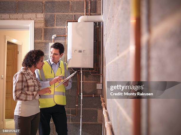 energy advisor discussing usage of energy efficient boiler with woman in home - caldeira imagens e fotografias de stock