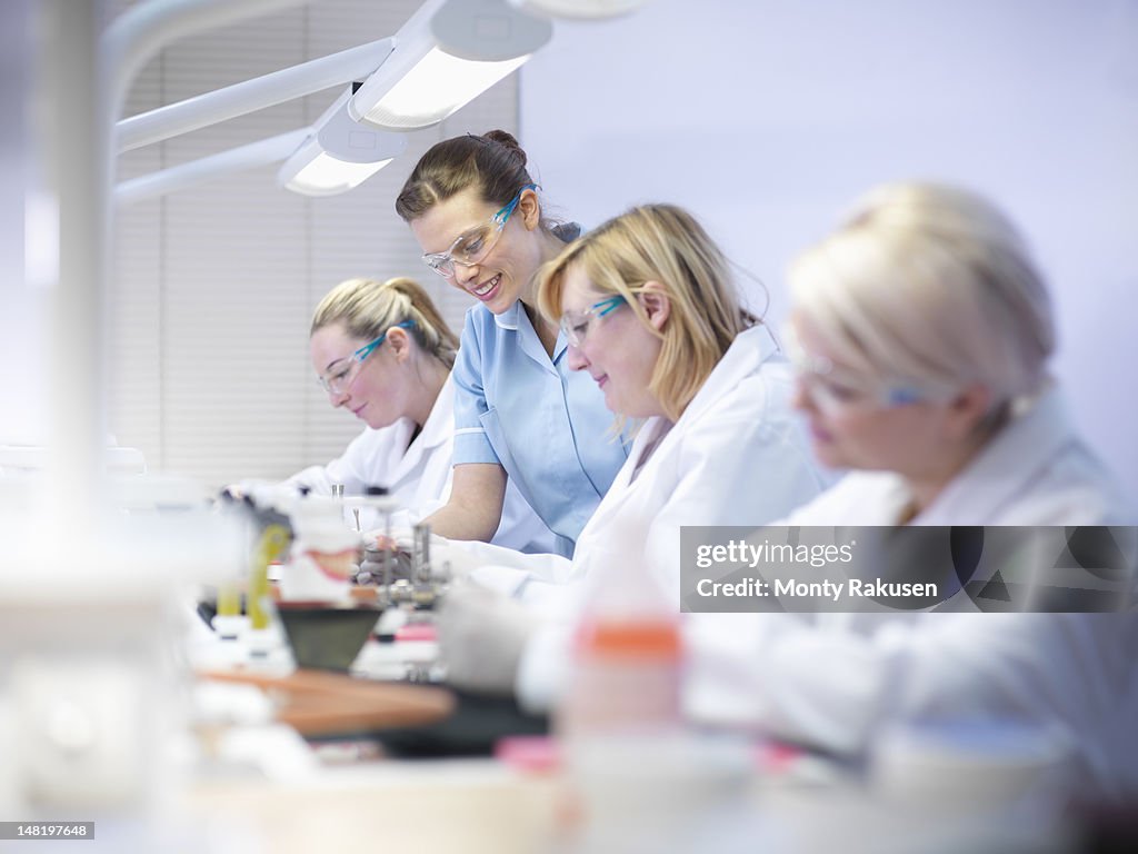 Professional dentist teaching apprentices in dental laboratory