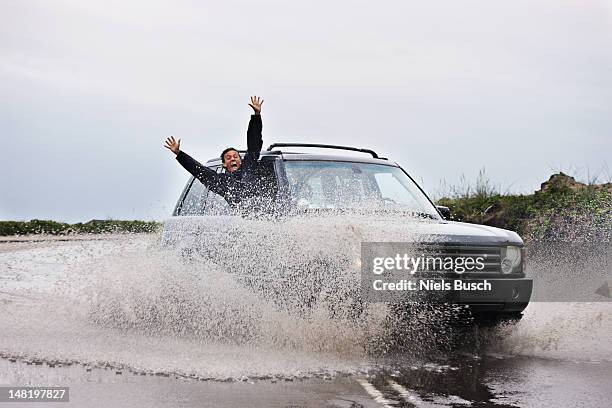 man leaning out of splashing car - car splashing stock pictures, royalty-free photos & images