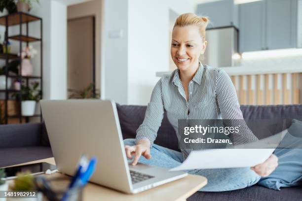 mature entrepreneur working from home on laptop, anaylzing documents and doing paperwork - filing documents stock pictures, royalty-free photos & images