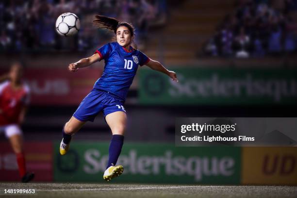 professional female soccer midfielder player jumps in the air as she prepares to kick a soccer ball into the goal - punting stock pictures, royalty-free photos & images
