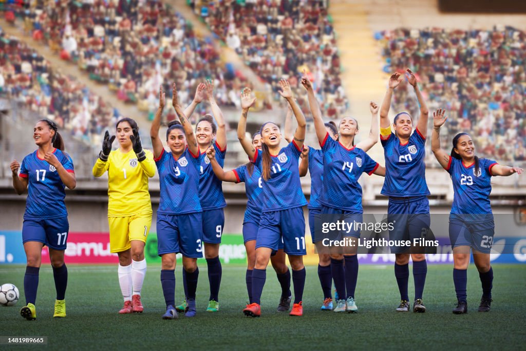 A group of young professional women soccer players celebrate and acknowledge their fans.