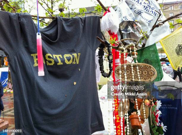 Close-up of various objects, including a T-shirt, flowers, rosaries, prayer flags, and a glow stick, at a memorial for the victims of the Boston...