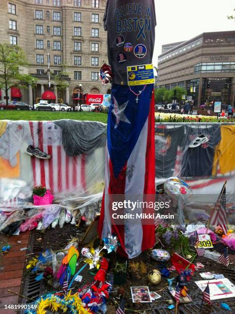 Close-up of various objects, including T-shirts, flowers, and American & Puerto Rican flags, at a memorial for the victims of the Boston Marathon...