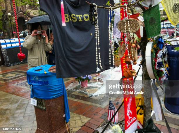 Close-up of various objects, including T-shirts, flowers, rosaries, prayer flags, and a glow stick, at a memorial for the victims of the Boston...
