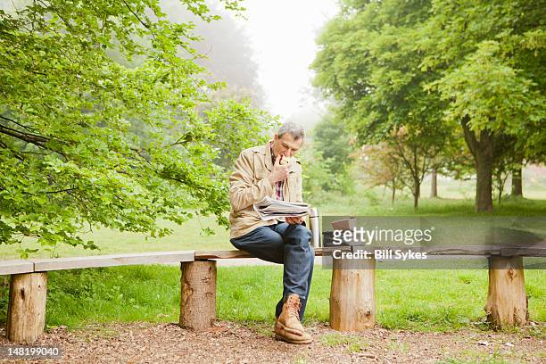 mann liest zeitung im park - bench park stock-fotos und bilder