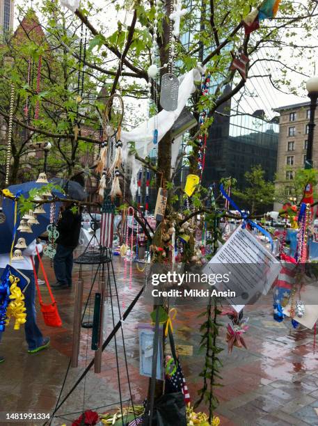 Close-up of various objects, including flowers, a dreamcatcher, dog tags, and wind chimes, at a memorial for the victims of the Boston Marathon...