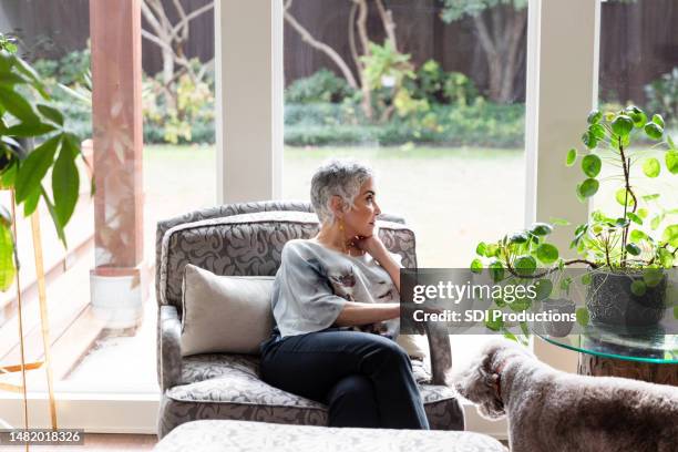 lonely grandmother looks out window of sunroom - depressed mother stockfoto's en -beelden