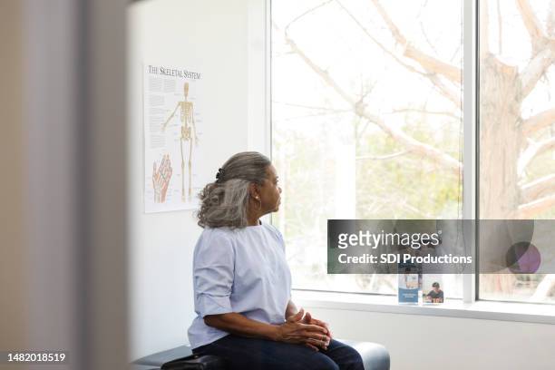 mujer adulta mayor mira por la ventana en el consultorio del médico - paciencia fotografías e imágenes de stock