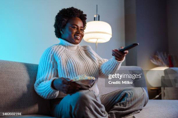 femme afro-américaine regardant l’émission de télévision préférée et mangeant du pop-corn à la maison - zapper photos et images de collection