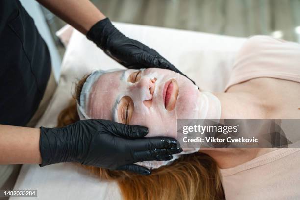 the cosmetologist applying a sheet mask to the face. - face lifting stock pictures, royalty-free photos & images