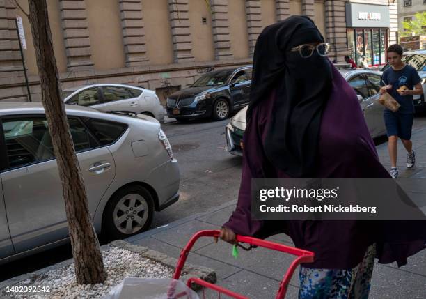 Muslim woman wearing a niqab pushes her cart along a sidewalk in New York City. A niqab has been considered to be an interpretation of women in the...