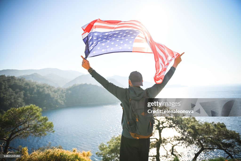 Mann mit amerikanischer Flagge auf dem Hintergrund des Meeres und der Berge