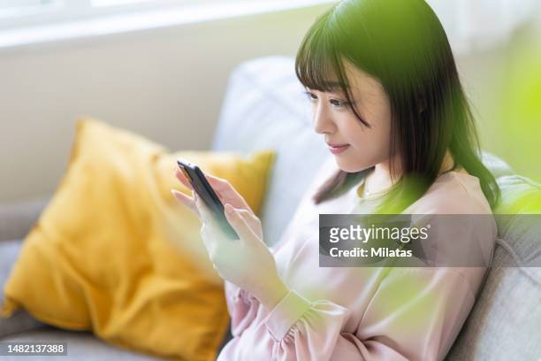 woman sitting on sofa and looking at smartphone - japanese woman bildbanksfoton och bilder