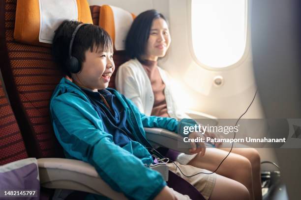 un buen servicio a bordo hace que viajar sea agradable. vista lateral de un niño asiático con auriculares y chaqueta sentado con su madre en el avión mirando la pantalla del monitor viendo dibujos animados durante el vuelo con sonrisa y felicidad. relac - aircraft wifi fotografías e imágenes de stock