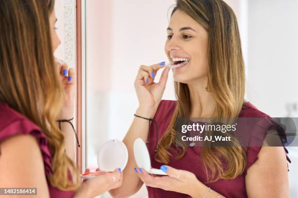 mujer joven con alineadores dentales mirándose en un espejo - odontología cosmética fotografías e imágenes de stock