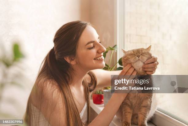 portrait of attractive smiling female fondling her cat. young woman in white top stroking grayish pet. - short game stock pictures, royalty-free photos & images