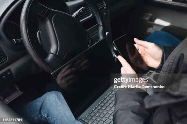 man with laptop and smartphone in car. chip tuning car systems - fachmann auto smartphone stock-fotos und bilder