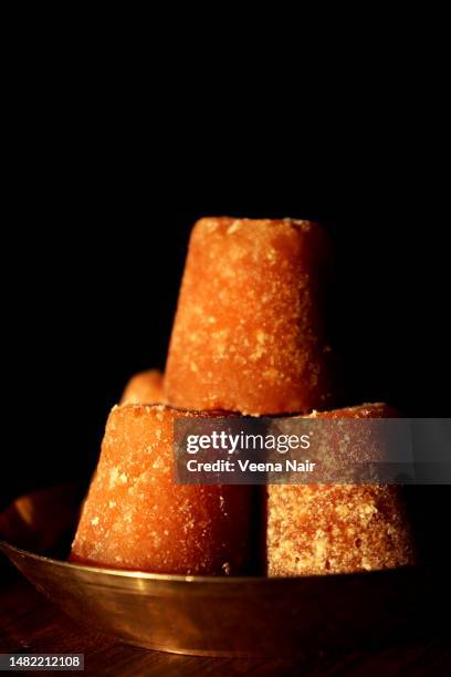 close-up of organic jaggery cubes in a brass plate on a wooden table against black background - jaggery stock pictures, royalty-free photos & images