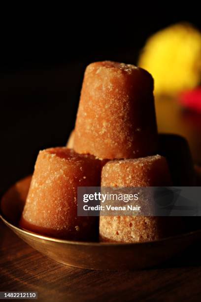 close-up of organic jaggery cubes in a brass plate on a wooden table against black background - jaggery stock pictures, royalty-free photos & images