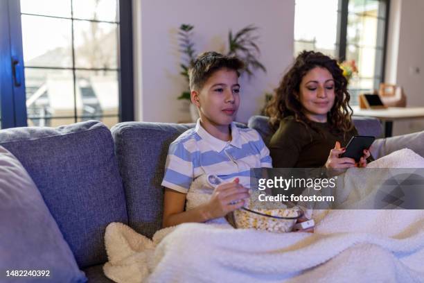 adolescente viendo televisión con su madre que está usando un teléfono inteligente - familia viendo la television fotografías e imágenes de stock