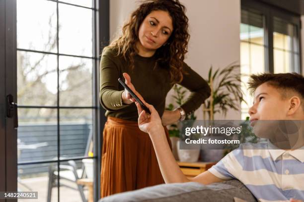 frau schimpft mit ihrem sohn im teenageralter, nimmt ihm sein smartphone weg und diszipliniert ihn - spielregeln stock-fotos und bilder