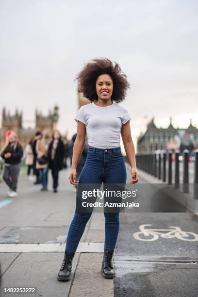 eine schöne erwachsene schwarze frau, die in die kamera lächelt, während sie auf einer brücke in london steht - person falls from westminster bridge stock-fotos und bilder