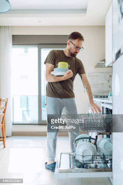 adult man unloading dishwasher machine - wasserglas stockfoto's en -beelden