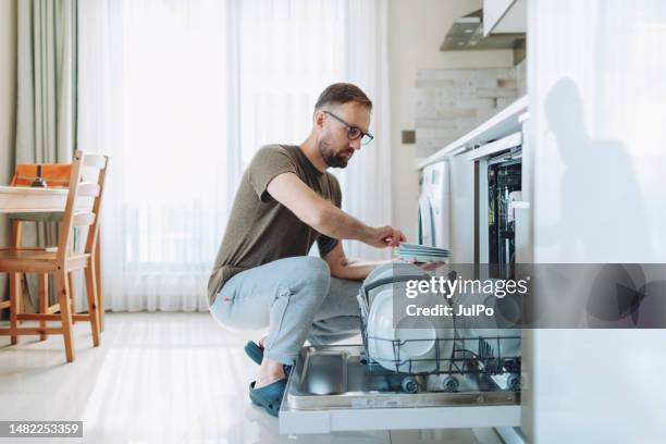 adult man unloading dishwasher machine - loading dishwasher stock pictures, royalty-free photos & images