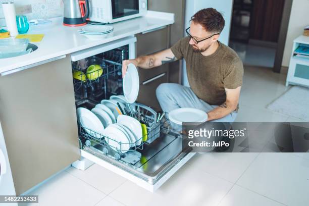 erwachsener mann entlädt spülmaschine - spülmaschine stock-fotos und bilder
