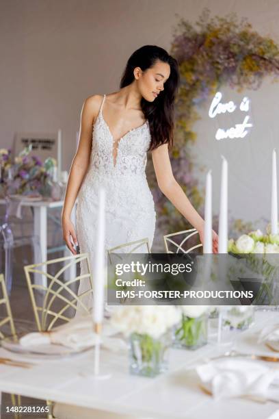 pretty young bride in her wedding dress looking at the table setting at her wedding venue. - banquet hall stock pictures, royalty-free photos & images