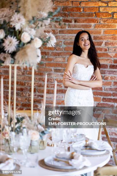 pretty young bride standing behind dinner table with her arms crossed looking at camera and smiling. - perfect moment stock pictures, royalty-free photos & images