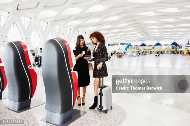 wide shot friends checking in at self service kiosk in airport - self service check in stock pictures, royalty-free photos & images