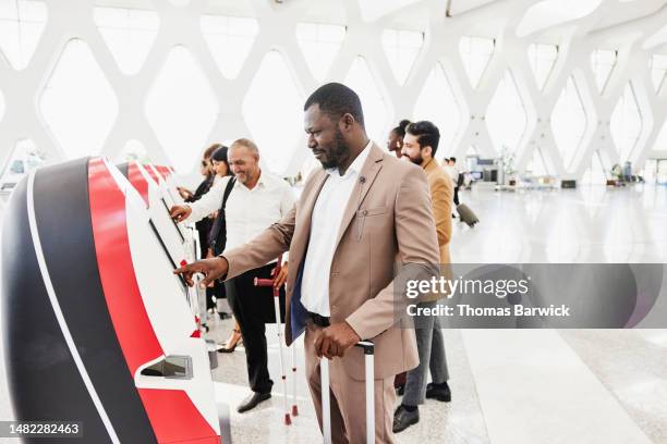 medium shot businessman checking in at self service kiosk in airport - self service stock pictures, royalty-free photos & images