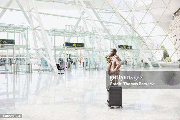 wide shot businessman taking on phone in airport arrivals after flight - wide shot stock pictures, royalty-free photos & images