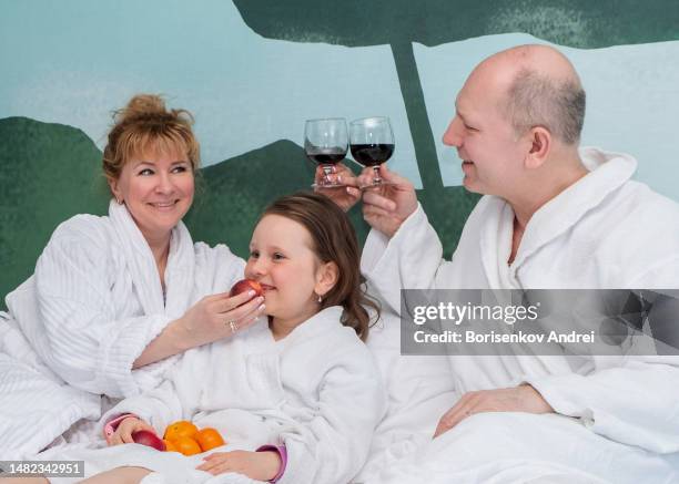 the family of caucasians is resting. a 50-year-old man, a 40-year-old woman and a 7-year-old girl in white coats are relaxing, drinking wine and eating fruit. - lebanon wine stock pictures, royalty-free photos & images