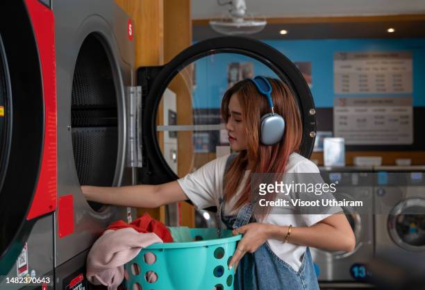 young woman loading a washing machine inside a laundromat shop. - money laundery stock pictures, royalty-free photos & images