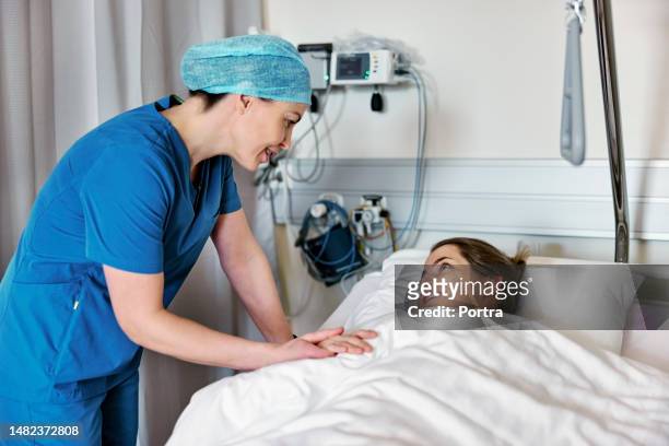 doctor comforting female patient lying on hospital bed - post operation stock pictures, royalty-free photos & images