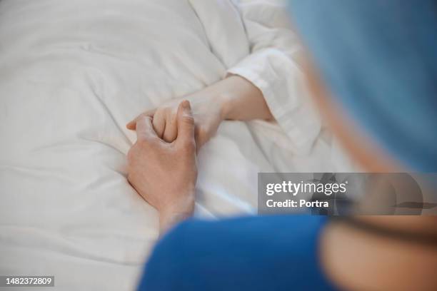 close-up of a doctor holding hand of a sick female patient on hospital bed - medical encouragement stock pictures, royalty-free photos & images