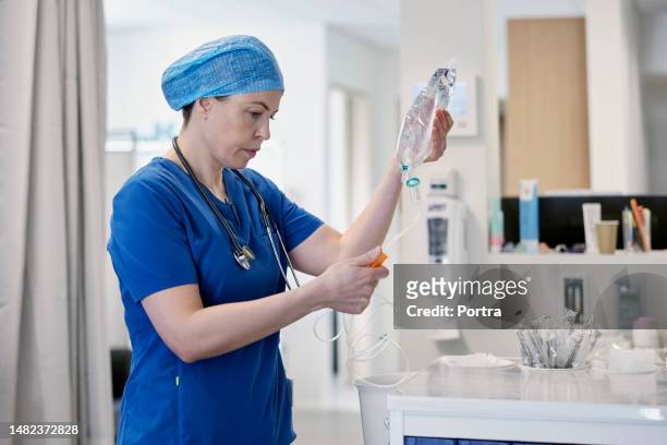 médico do sexo feminino preparando um gotejamento iv para o paciente na sala de emergência - infused - fotografias e filmes do acervo