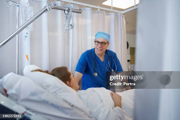 smiling male doctor attending sick woman in hospital ward - bedside manner stock pictures, royalty-free photos & images