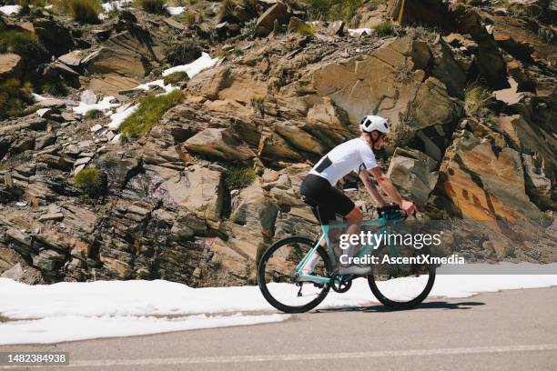 road cyclist rides up snowy mountain road - road cycling stock pictures, royalty-free photos & images