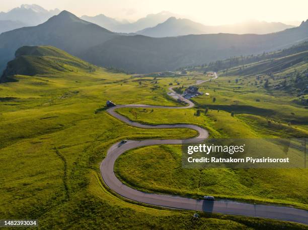 aerial view of a road winding through a dense green forest in dolomites national park, drone panoramic photo of the beautiful mountain pass hidden in the autumnn pine forest with the soft light of the autumn sunset, dolomites alps, south tyrol, italy - bergstrecke stock-fotos und bilder